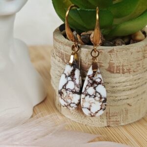 Boucles d’oreilles artisanales en magnésite naturelle blanche, montées sur crochets dorés, posées devant une plante verte.